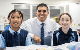 Two Our Lady of Mt Carmel School students and their teacher in front of books